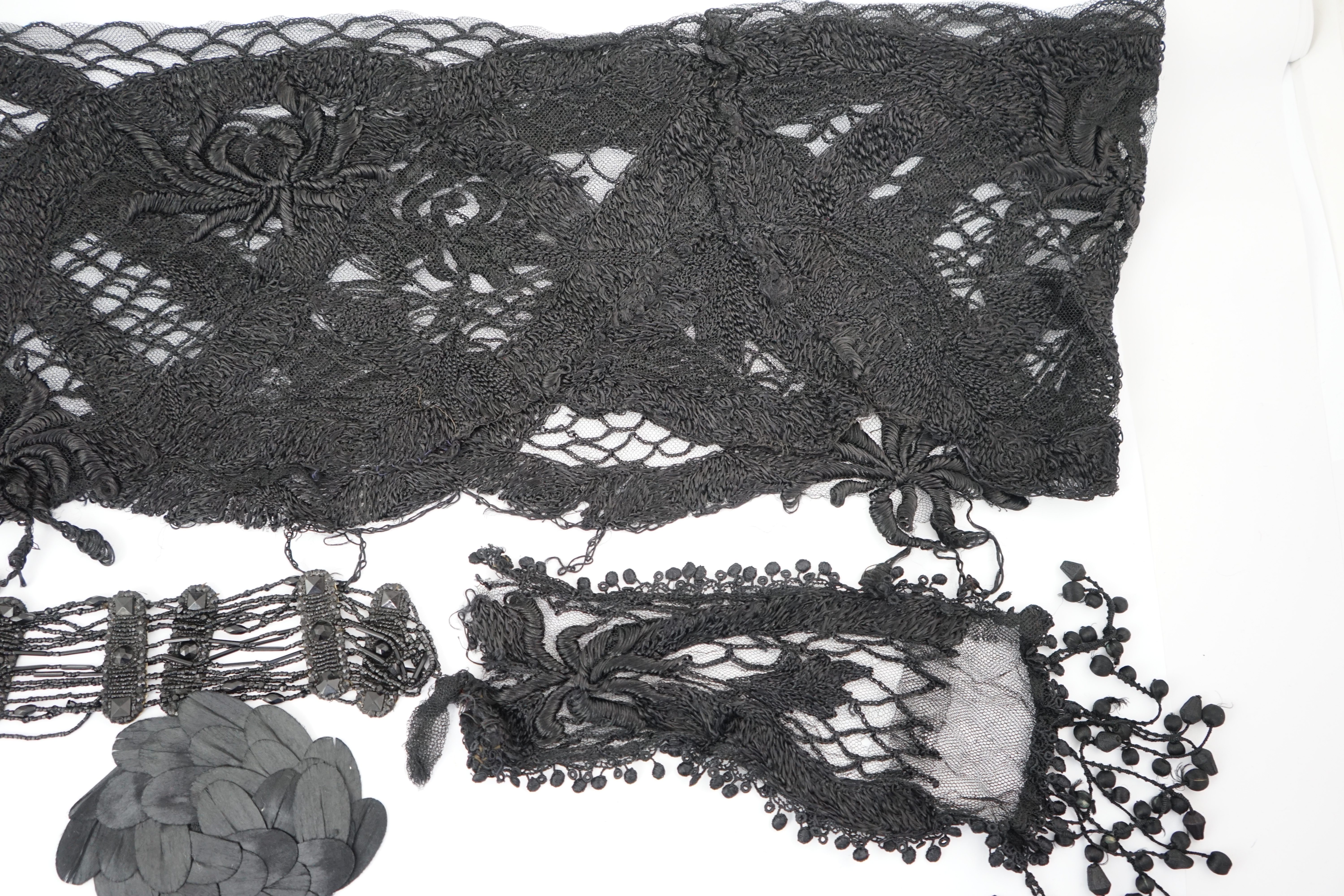 An 1930's black sequin cape, trimmings and lace, an Art Deco black sequin decorated cape on black net, an Edwardian jet beaded belt, a Spanish silk fall cap, three panels of black machine lace, a long length black and cr